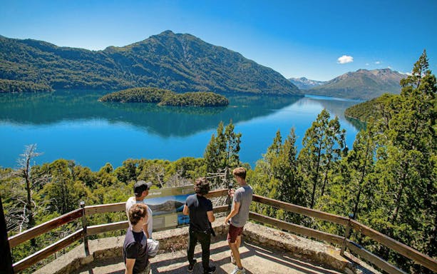 Visitors admiring Lake Mascardi and Patagonian mountains from a scenic viewpoint.