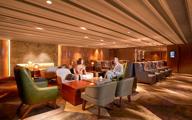 First-Class Lounge seating area at Hong Kong International Airport with travelers conversing.