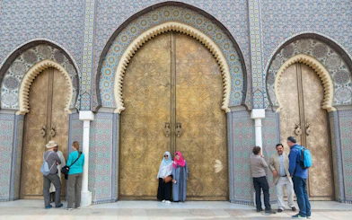 Golden doors with intricate patterns at the Royal Palace in Fes, Morocco, with visitors nearby.