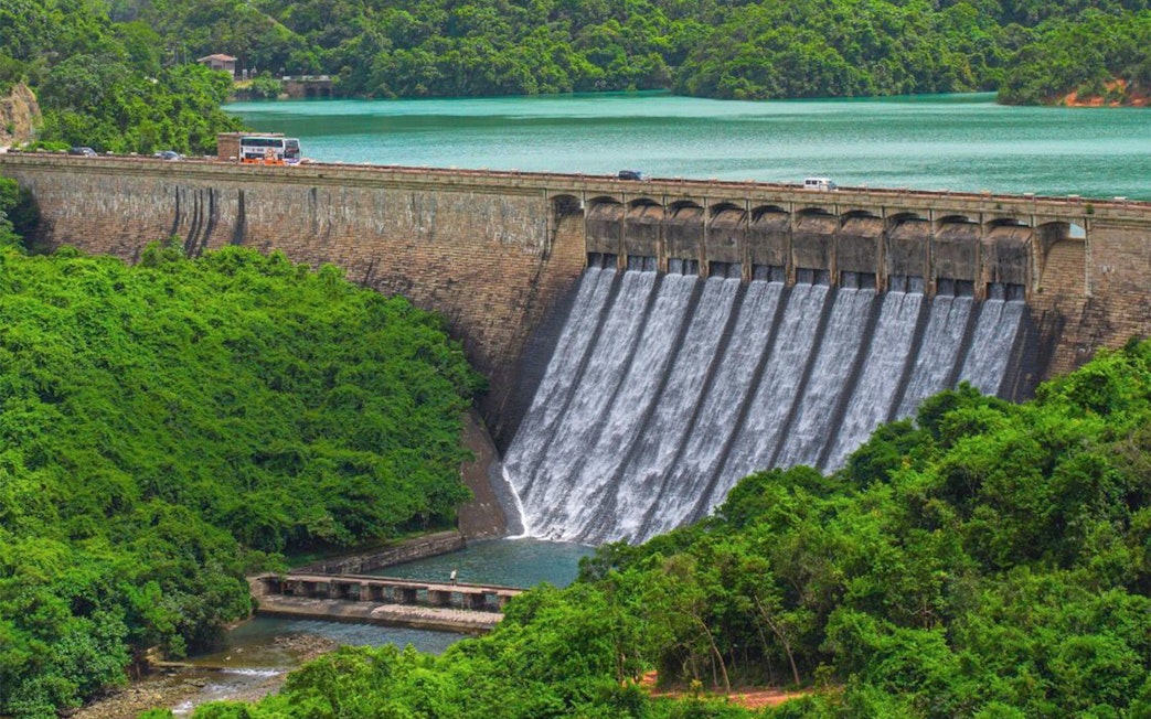 Big Bus tour passing over a dam with cascading water and lush greenery.
