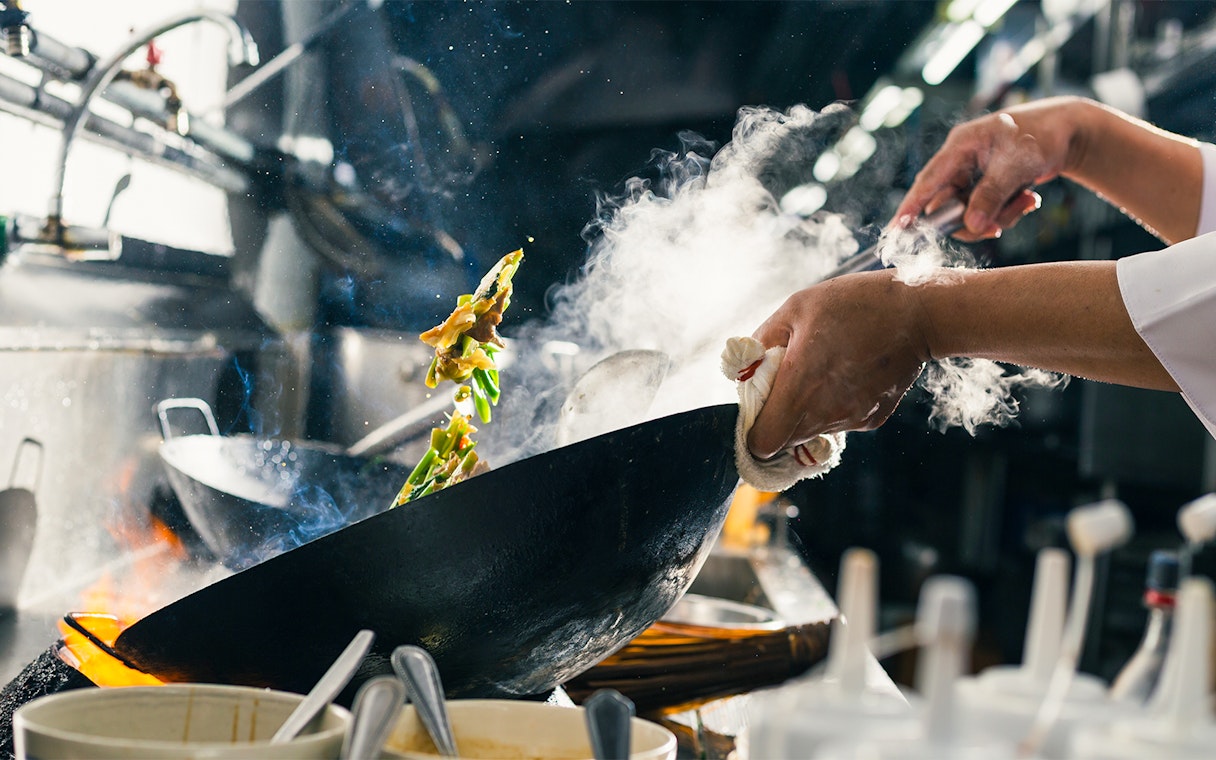 Chef stir-frying vegetables in a wok at a Sentosa Island restaurant kitchen.
