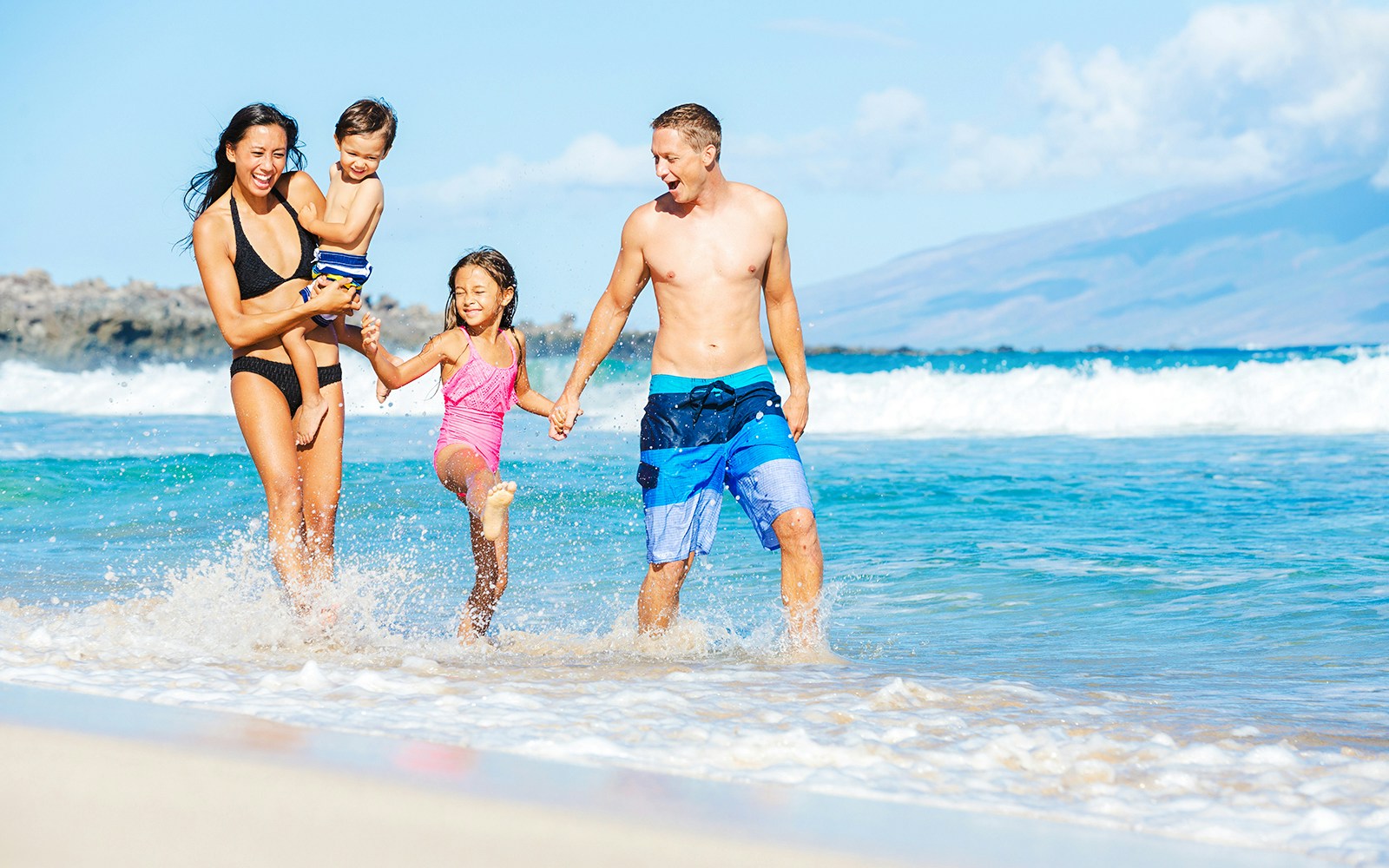 Family enjoying a sunny day at the beach with ocean waves in the background.