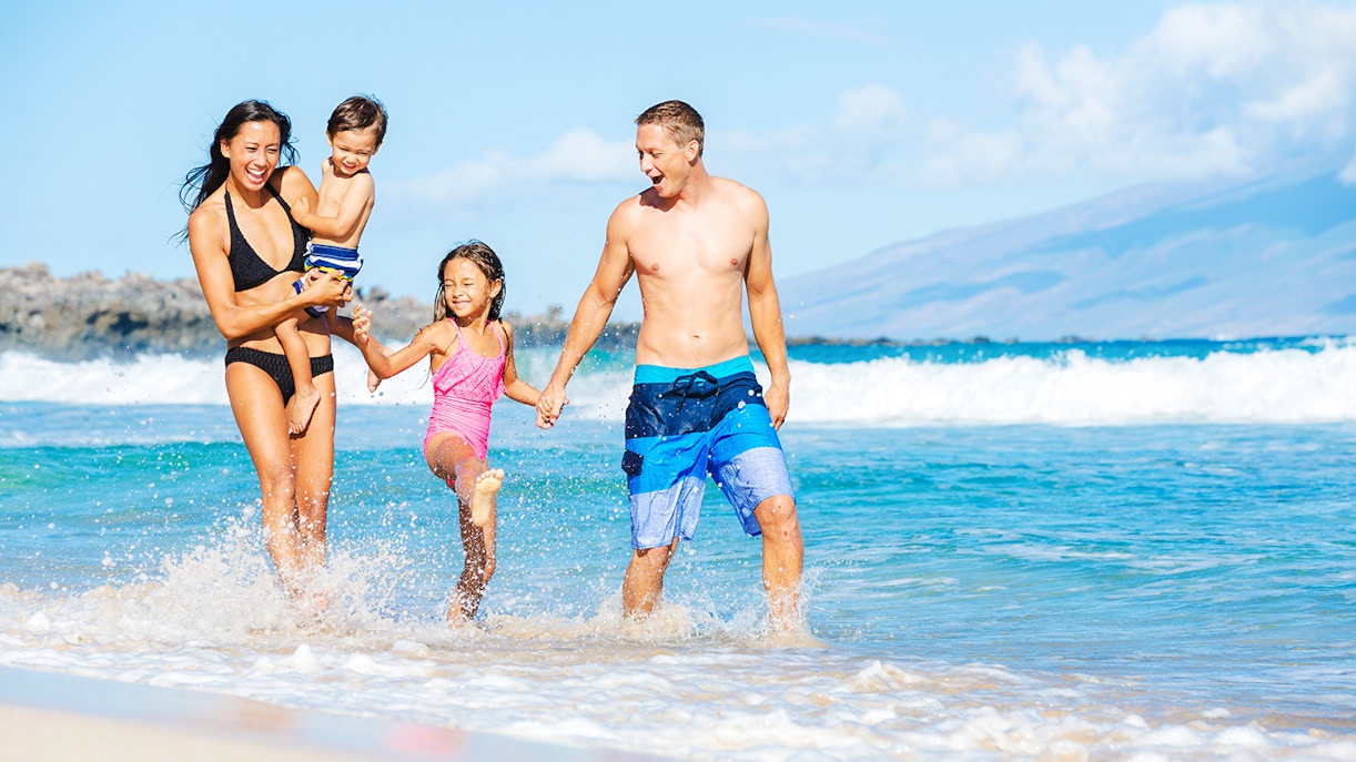 Family enjoying a sunny day at the beach with ocean waves in the background.