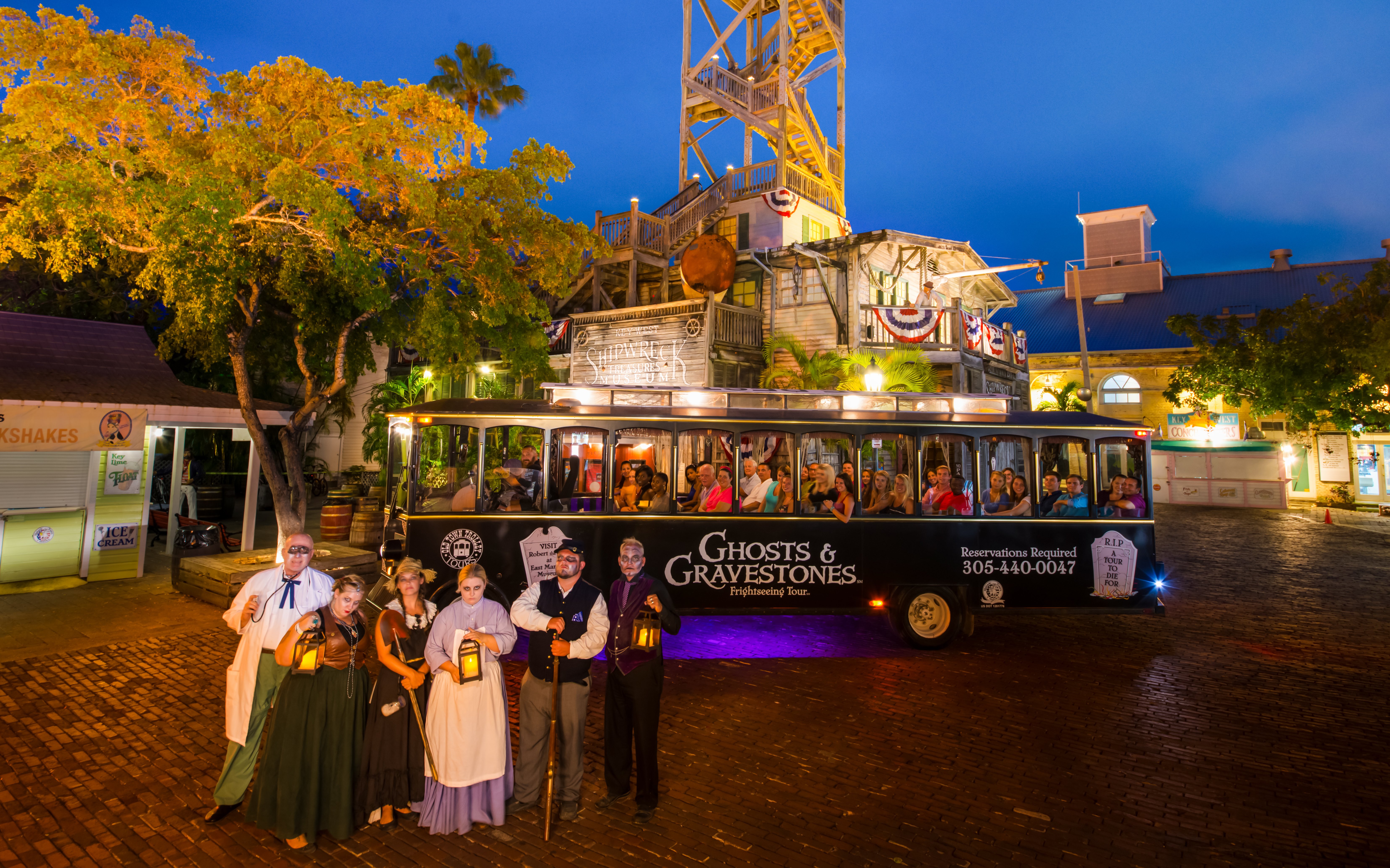 Ghosts & Gravestones tour trolley with costumed guides at night, historic building in background.