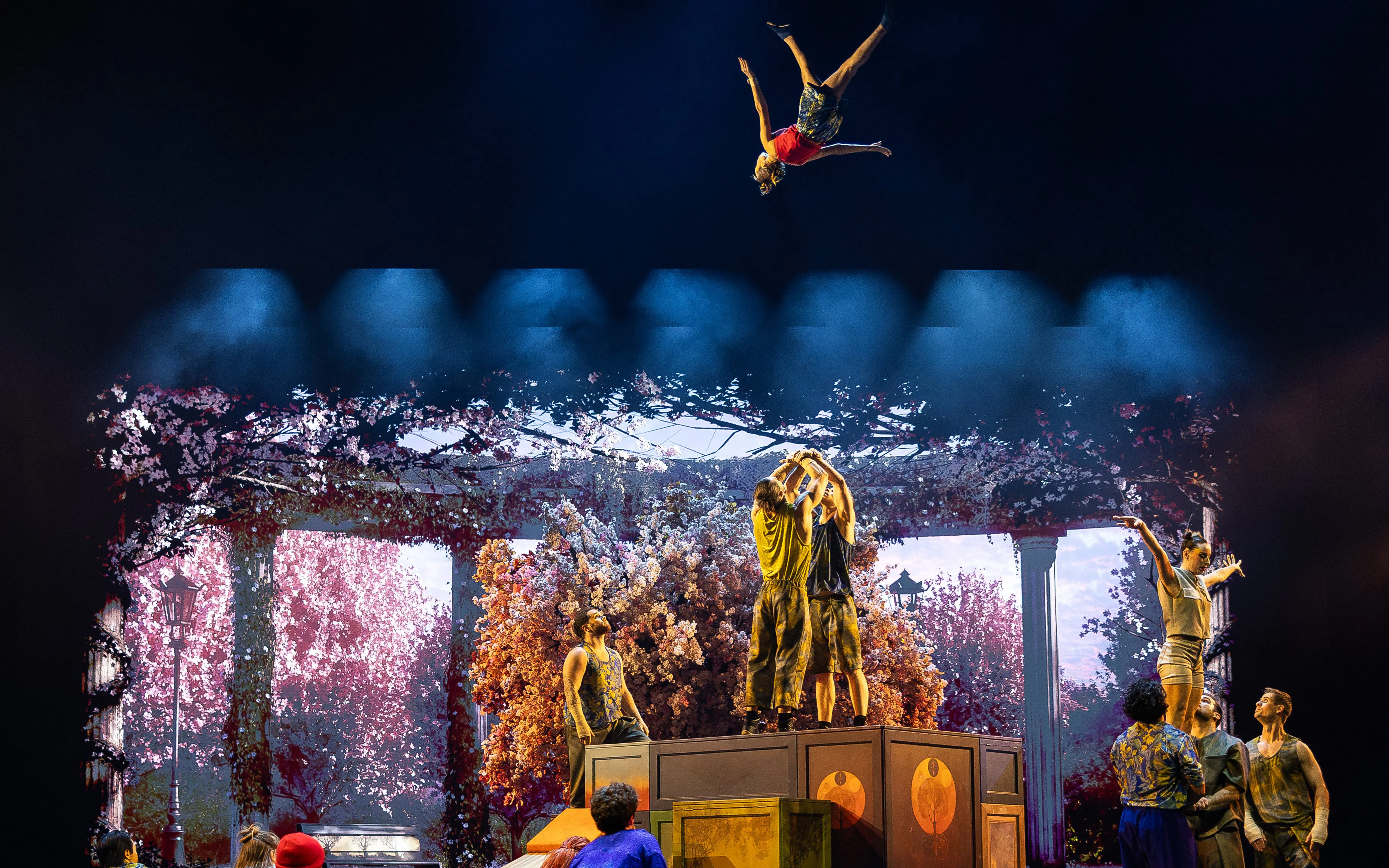 Acrobats performing mid-air flips during Cirque du Soleil Alizé stage show.