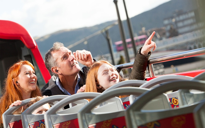 Family enjoying Edinburgh Hop-On Hop-Off bus tour, pointing at city sights.