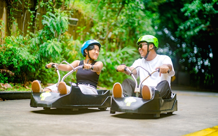 Couple enjoying Skyline Luge ride in Singapore amidst lush greenery.