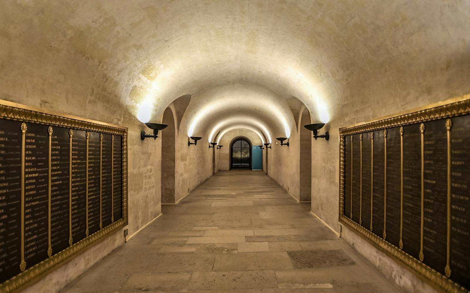 Crypt corridor with illuminated arches and memorial plaques in Paris Pantheon.