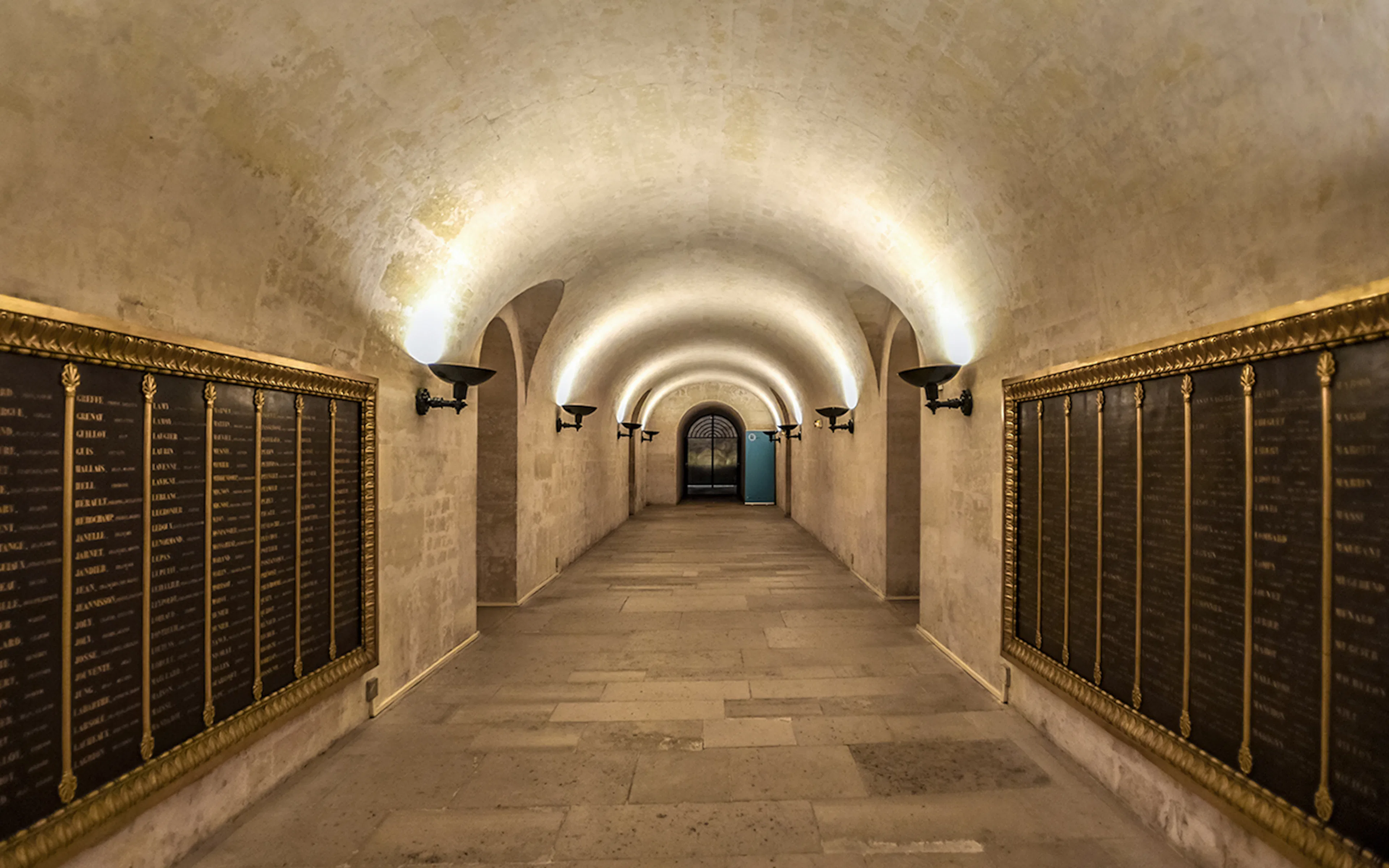 Crypt corridor with illuminated arches and memorial plaques in Paris Pantheon.