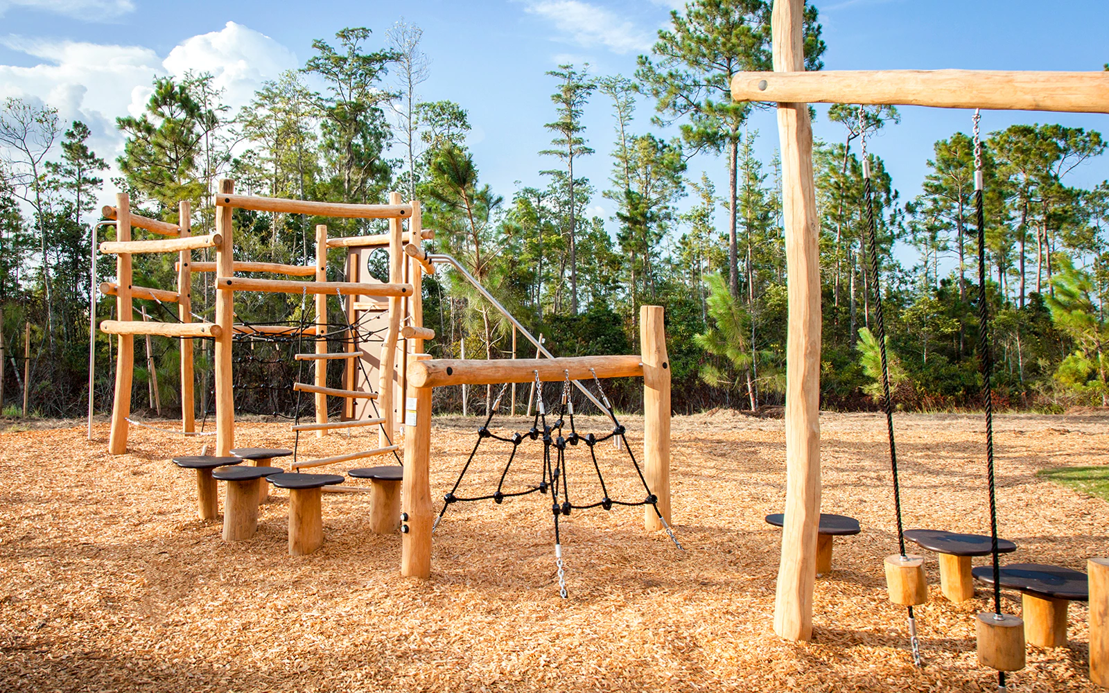 Wooden playground with climbing structures and swings in a forest setting.