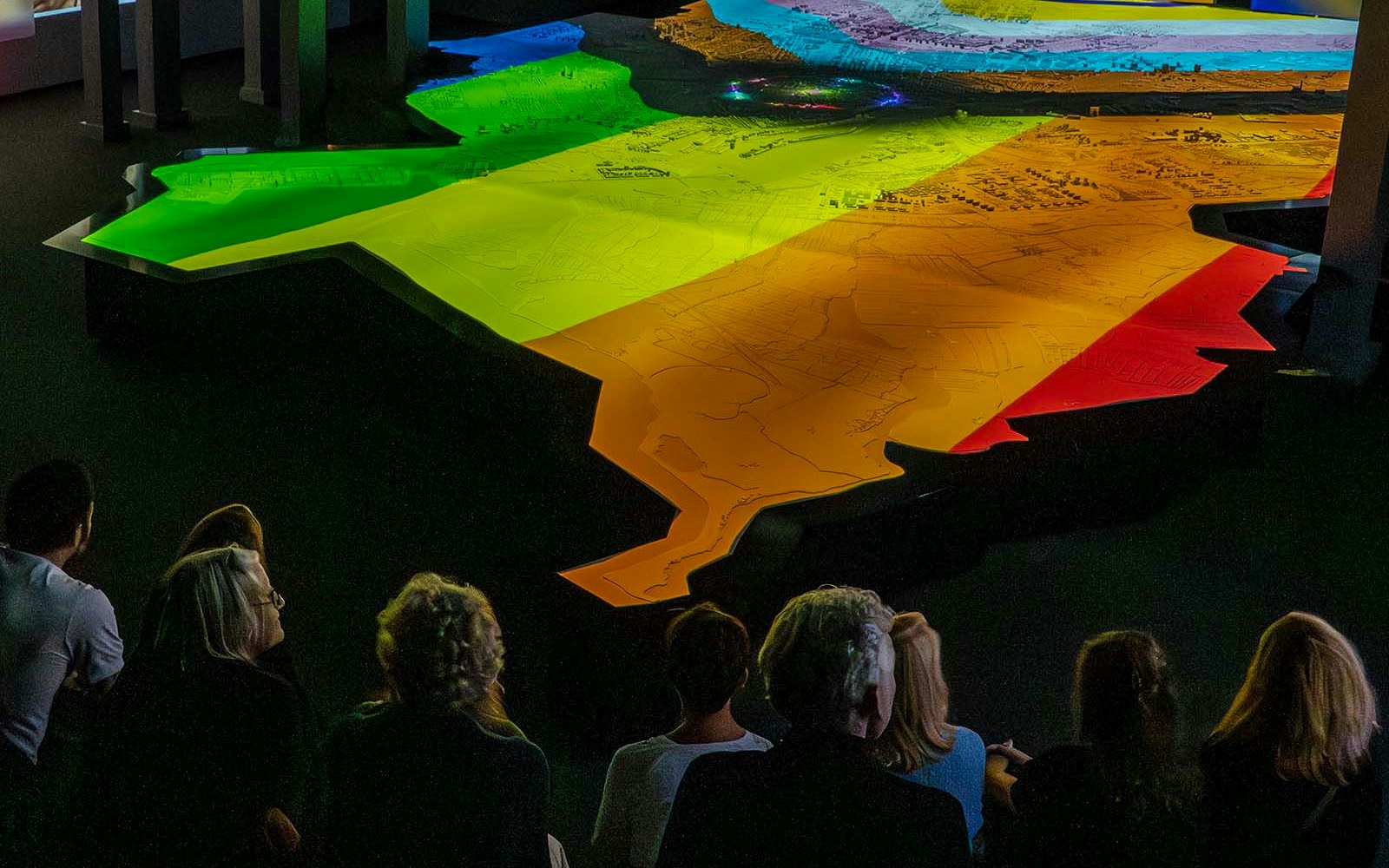 Visitors observing a colorful topographic map at the Amsterdam in Motion exhibit.