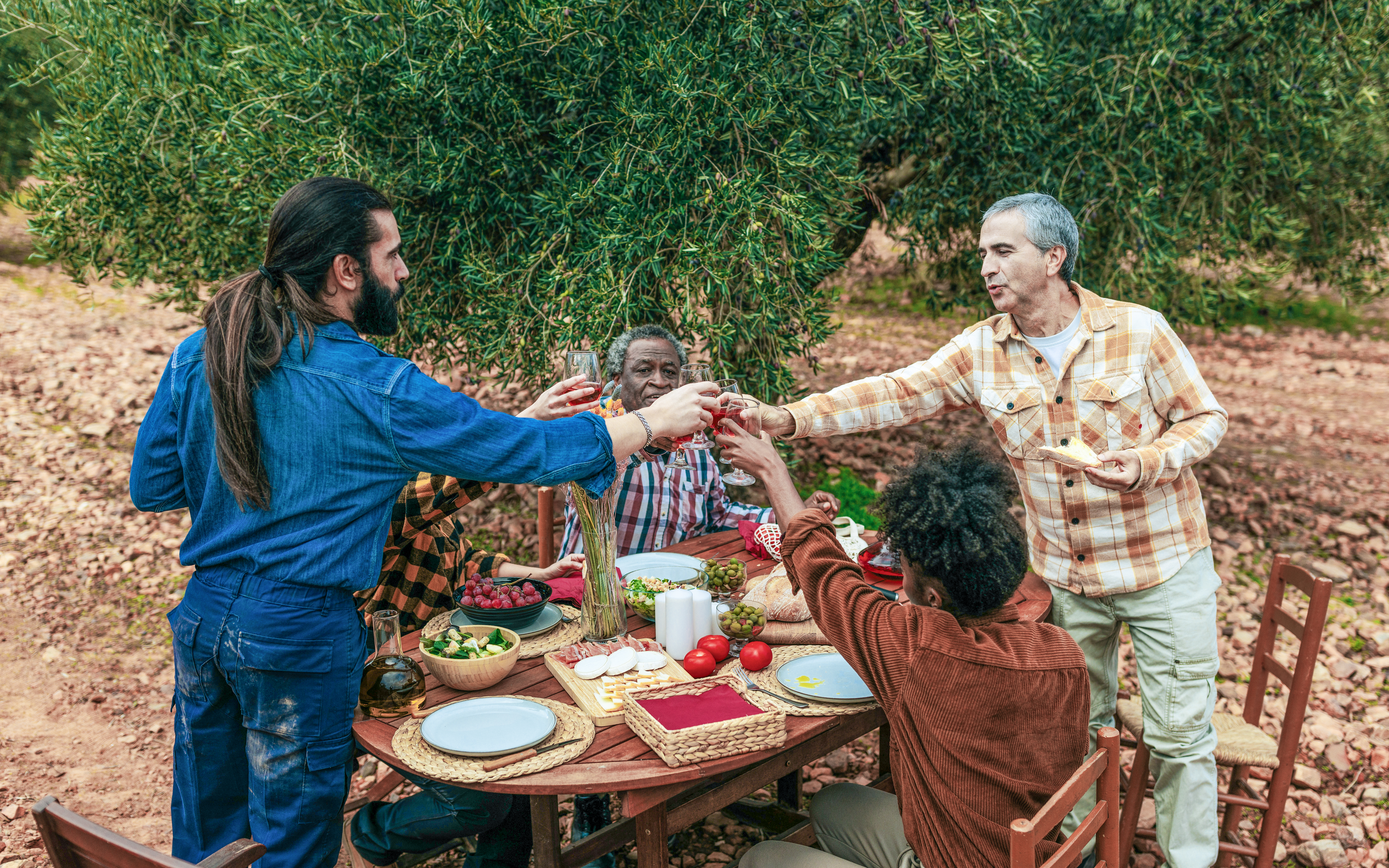 Farmers toasting with red wine in an olive grove after olive harvest.