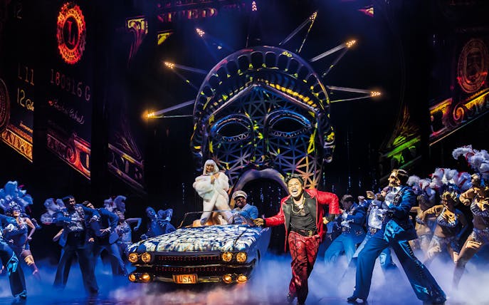 Stage performance of Miss Saigon with dancers and Statue of Liberty backdrop.