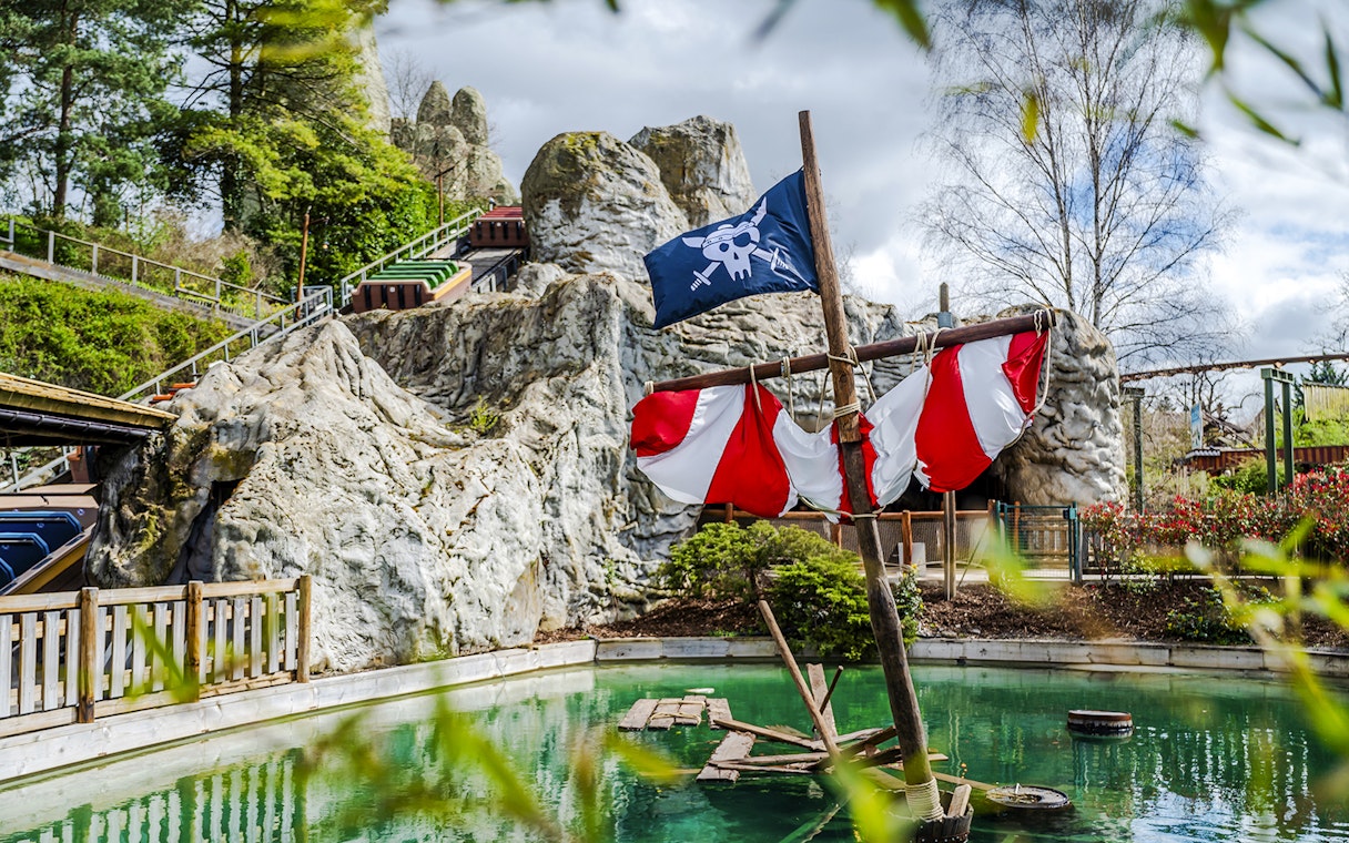 Pirate ship ride at Parc Asterix with rocky backdrop and green water.