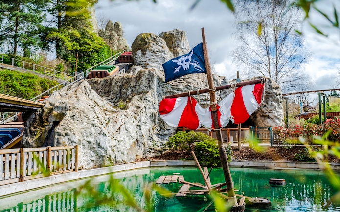 Pirate ship ride at Parc Asterix with rocky backdrop and green water.