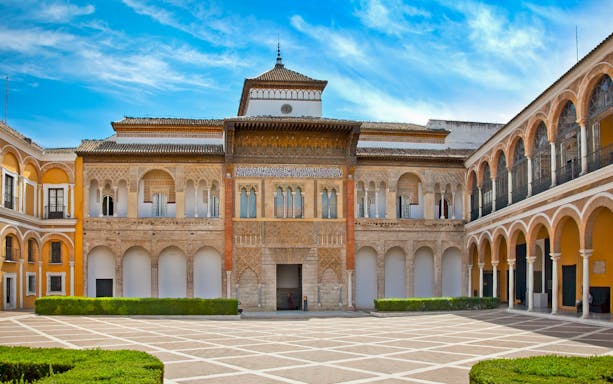 Courtyard view of Alcázar Seville with intricate arches and lush gardens.