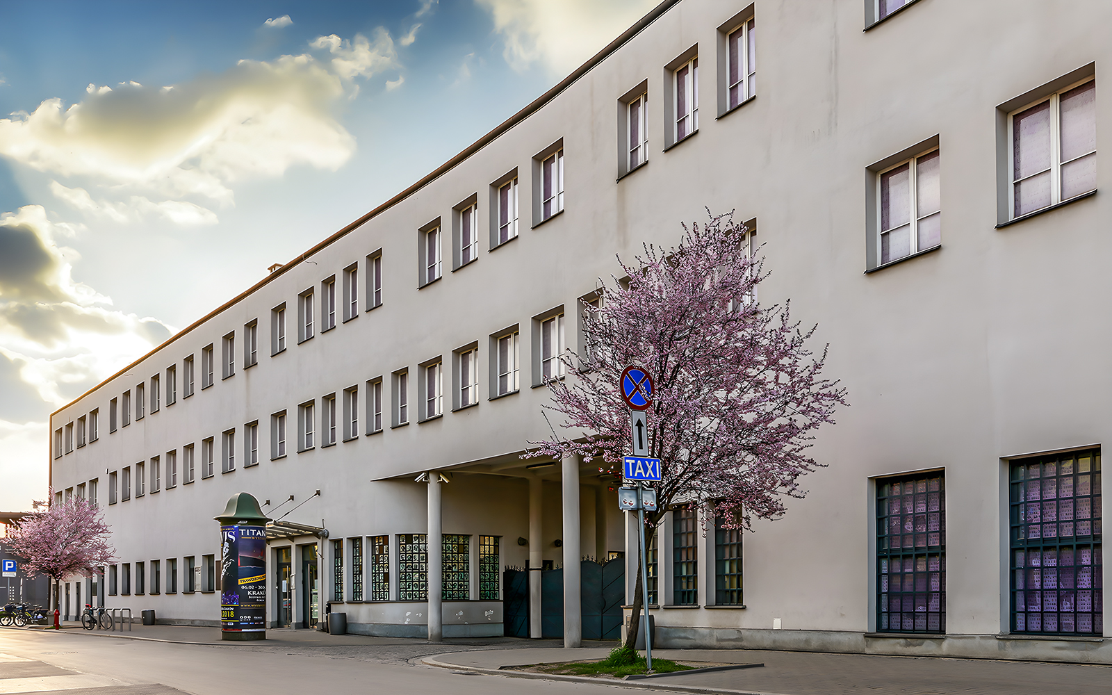 Schindler's Factory building in Krakow with blooming trees and street signs.