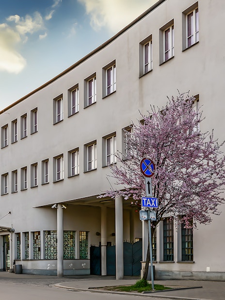 Schindler's Factory building in Krakow with blooming trees and street signs.