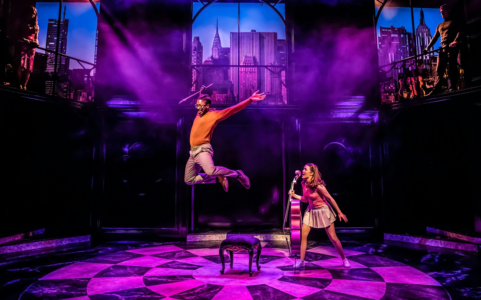 Performer jumping on stage during Cruel Intentions: The 90's Musical with cityscape backdrop.