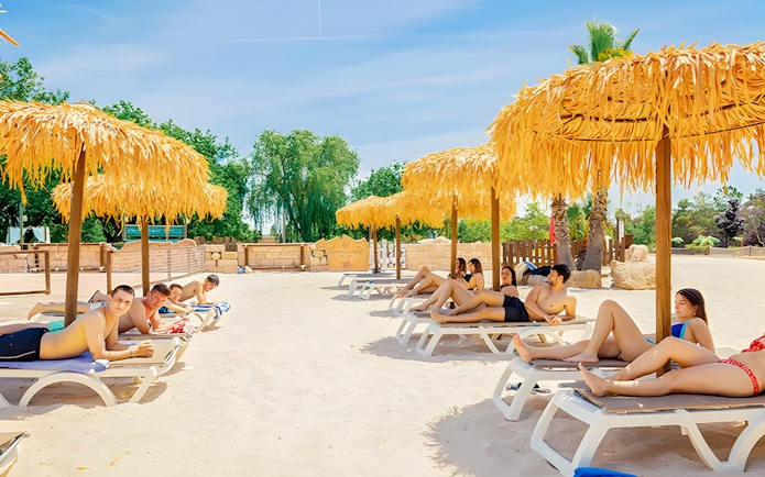 Visitors relaxing on sun loungers under straw umbrellas at Aquopolis Villanueva de la Cañada.