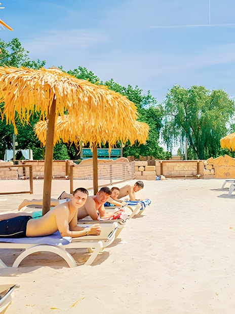 Visitors relaxing on sun loungers under straw umbrellas at Aquopolis Villanueva de la Cañada.