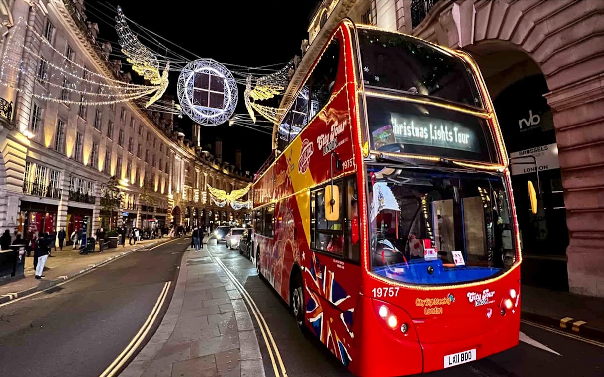 Red double-decker bus on London Christmas Lights Tour under festive street decorations.