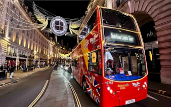 Red double-decker bus on London Christmas Lights Tour under festive street decorations.