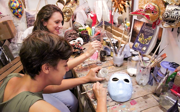 Participants painting masks at a workshop table with various art supplies.