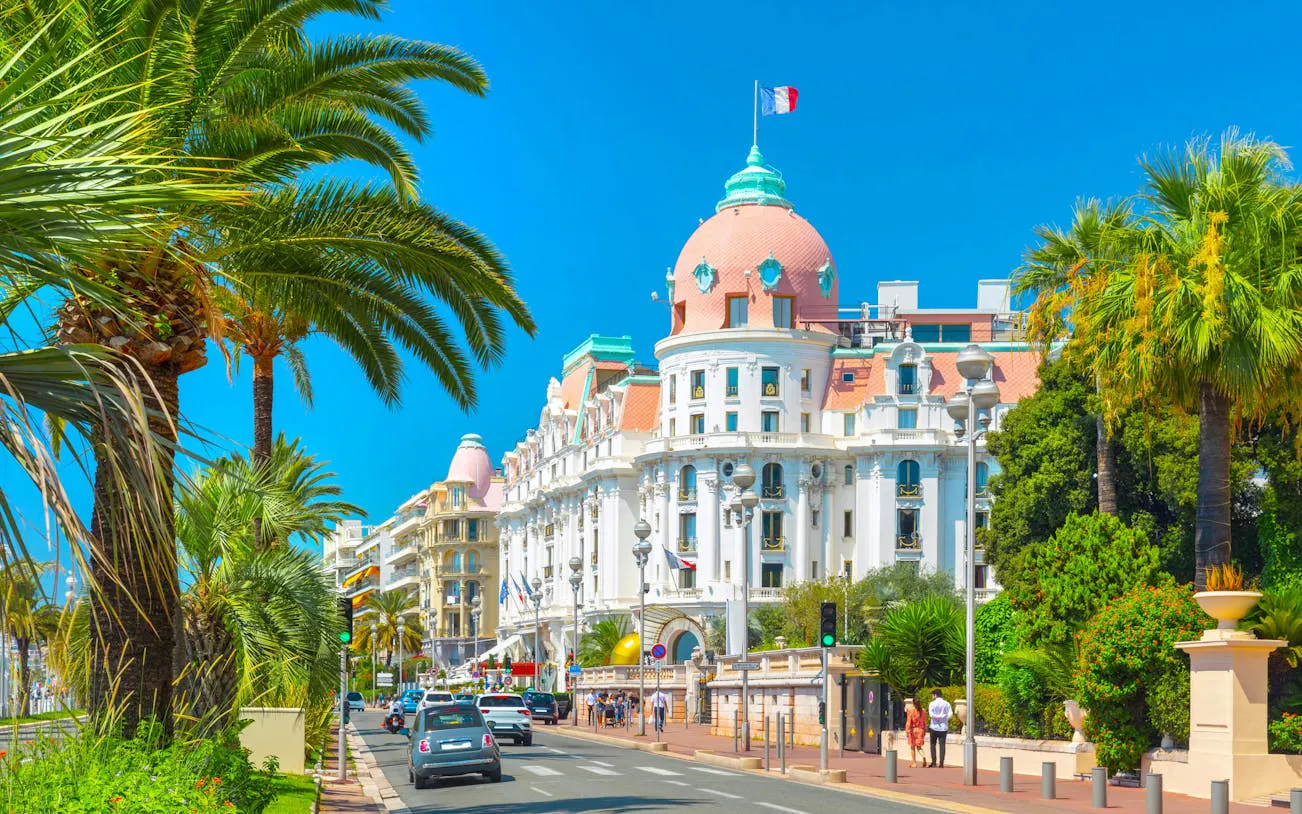Promenade des Anglais with palm trees and historic hotel in Nice, France.