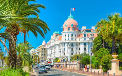 Promenade des Anglais with palm trees and historic hotel in Nice, France.