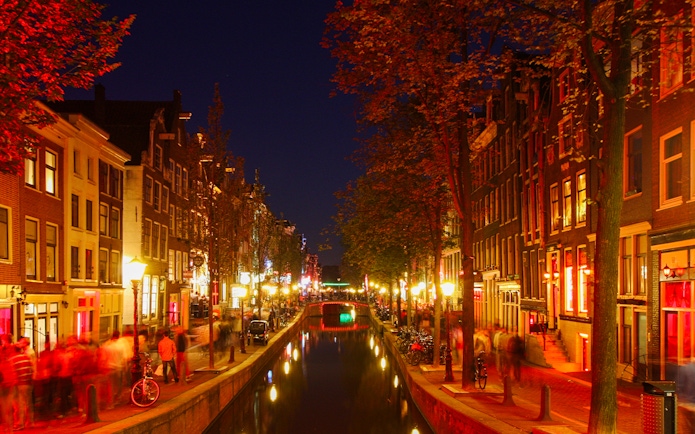 Amsterdam's red light district at night with illuminated canal and buildings.