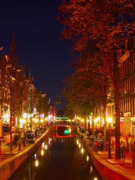 Amsterdam's red light district at night with illuminated canal and buildings.