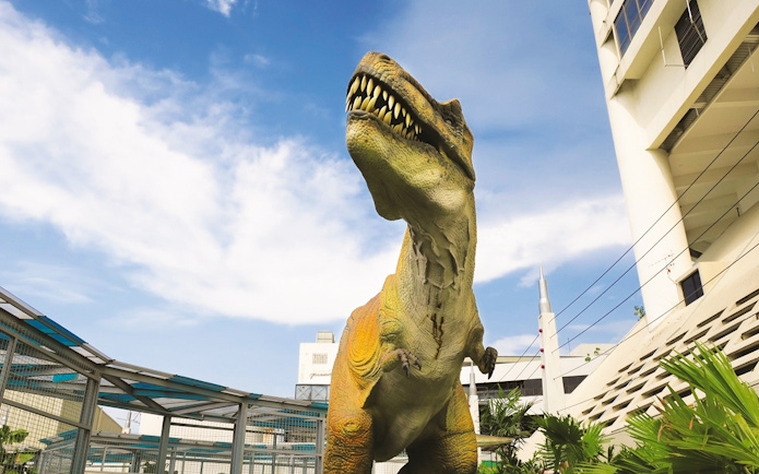 Dinosaur statue at Jurassic Research Centre with buildings in the background.