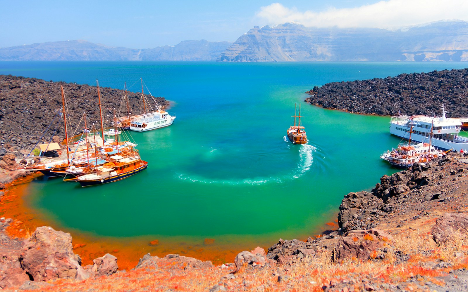 Nea Kameni volcanic island with tourists exploring the rocky terrain in Santorini.