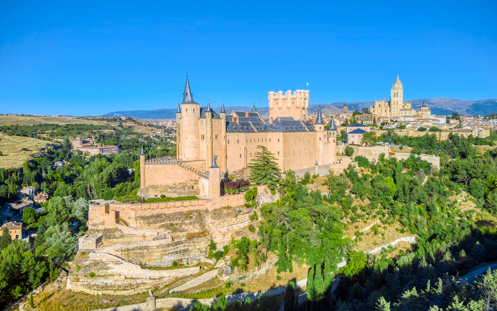 Aerial view of the Alcazar of Segovia, Spain, surrounded by lush greenery.