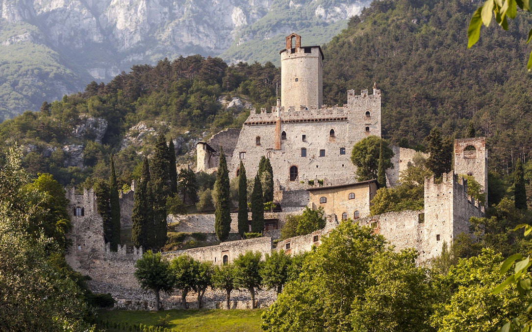Avio Castle surrounded by lush greenery and mountains in Trentino, Italy.