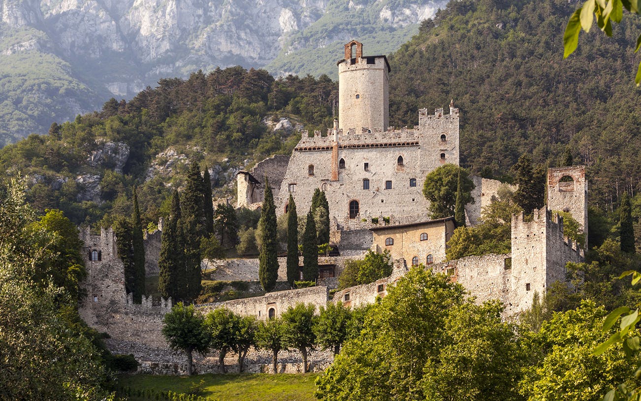Avio Castle surrounded by lush greenery and mountains in Trentino, Italy.