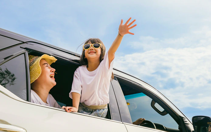 Family enjoying private car transfer with child leaning out window.