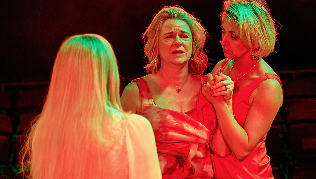 Three women in red dresses performing a dramatic scene in "Till The Stars Come Down" play.