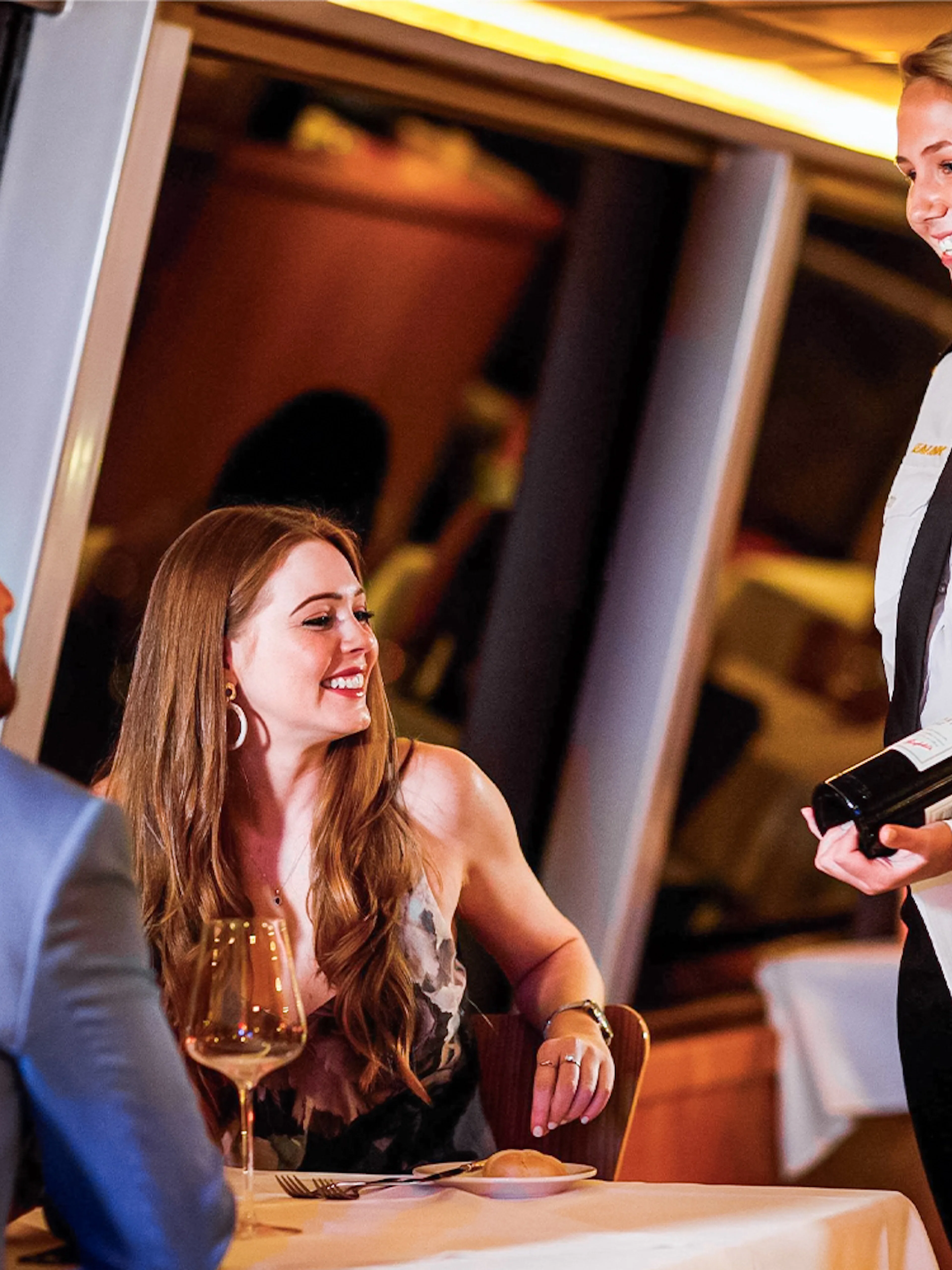 Couple dining on Sydney Harbour cruise with server presenting wine.