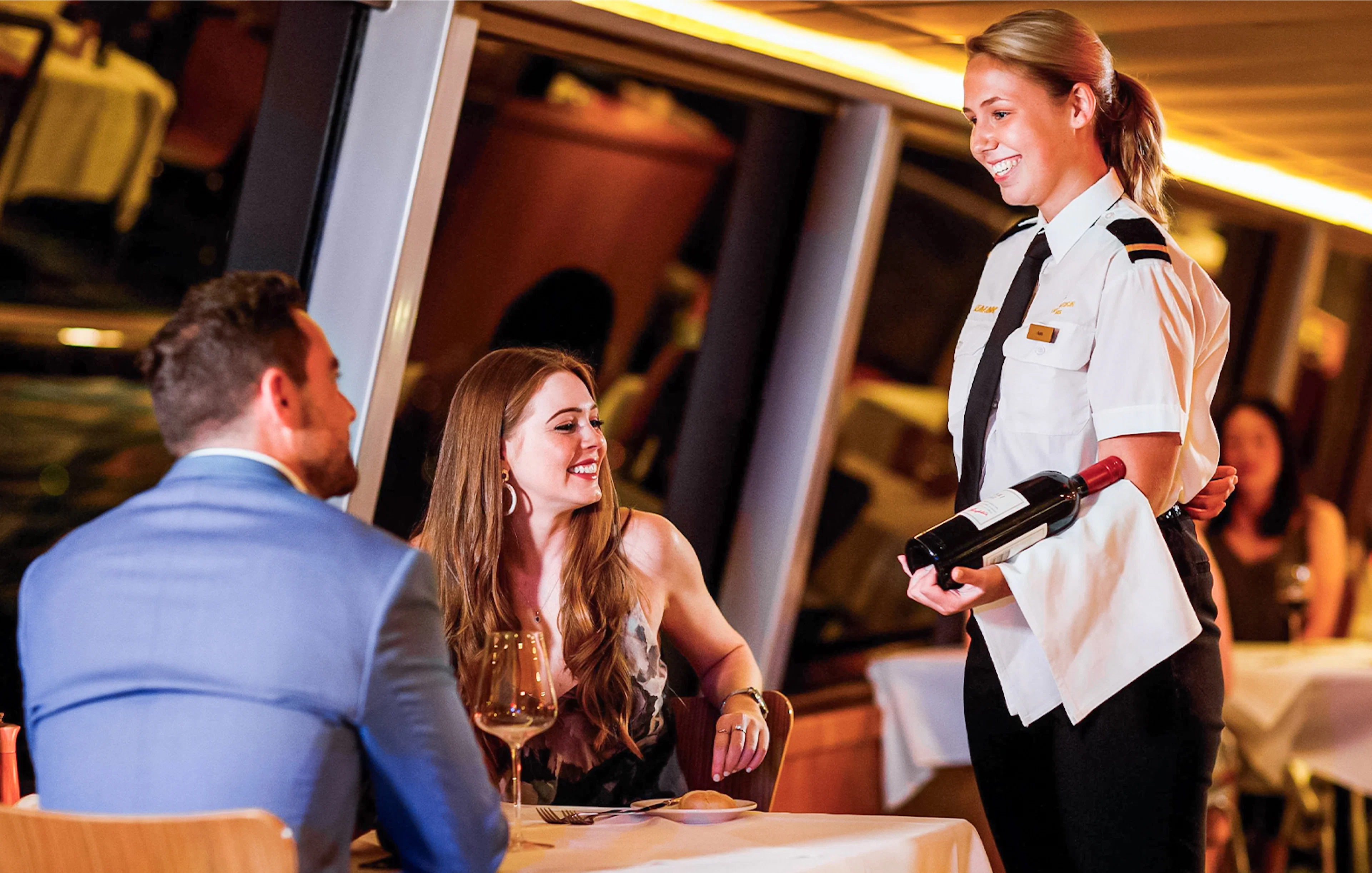 Couple dining on Sydney Harbour cruise with server presenting wine.