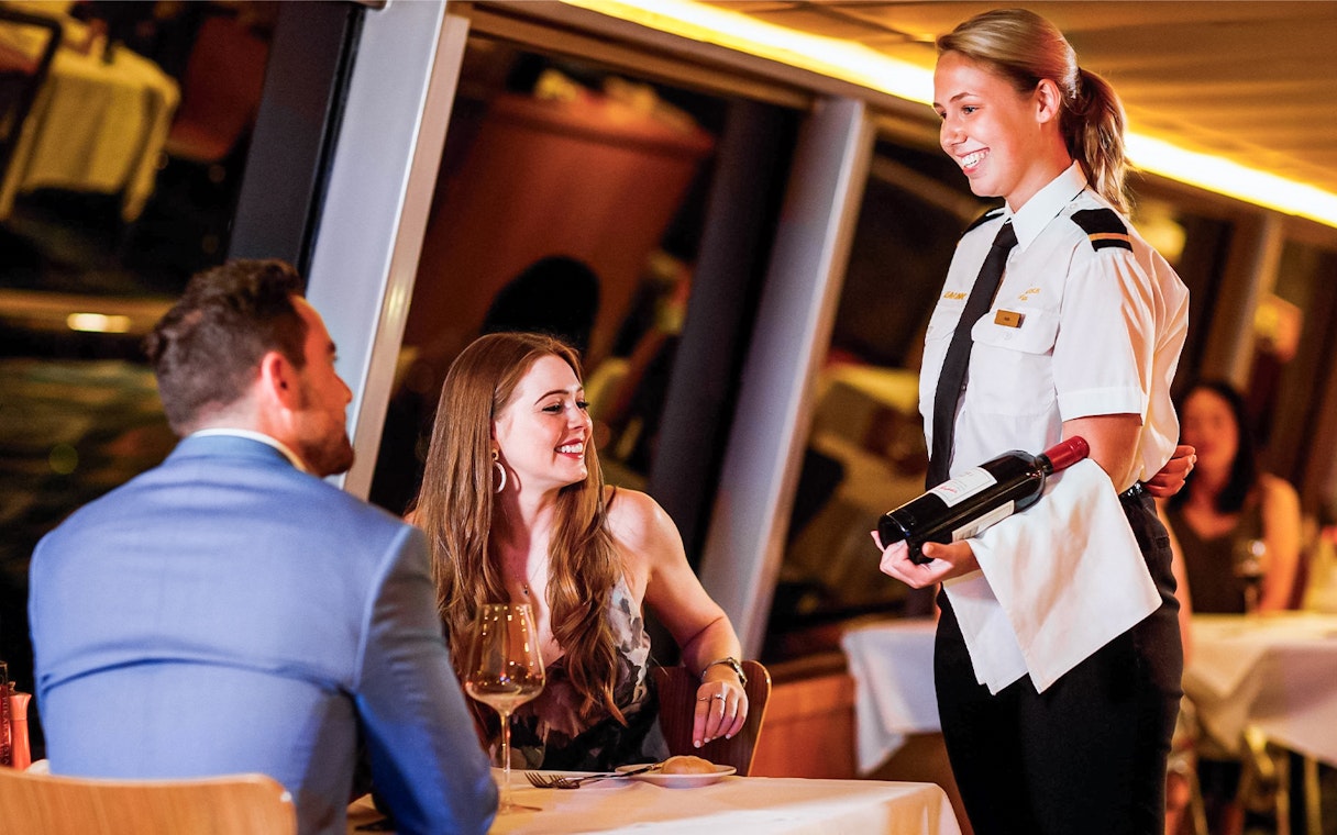 Couple dining on Sydney Harbour cruise with server presenting wine.