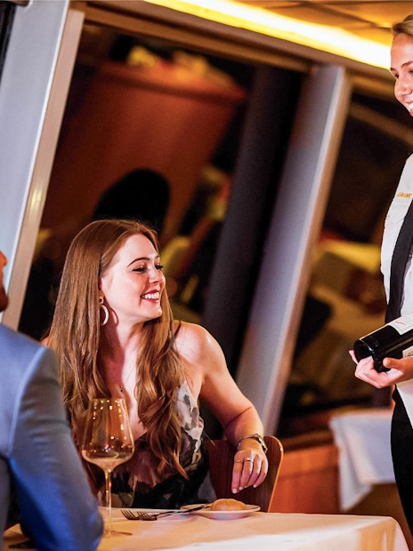 Couple dining on Sydney Harbour cruise with server presenting wine.
