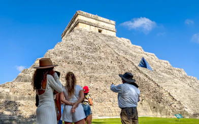 Tourist guide explaining Chichen Itza temple to visitors under a clear blue sky.