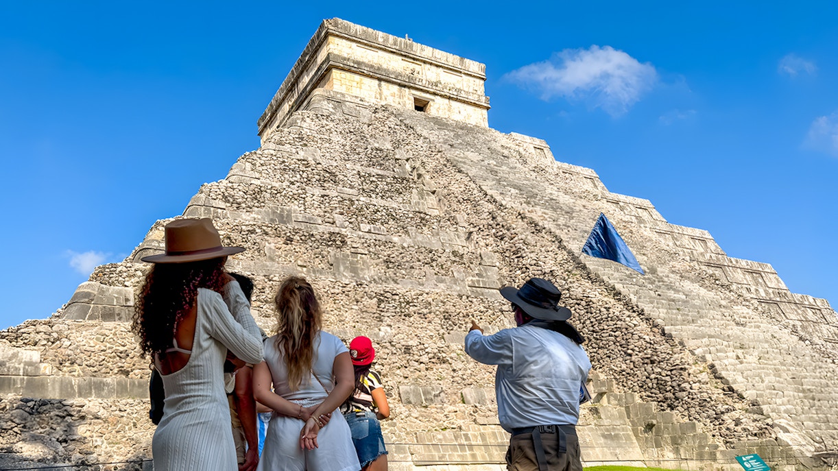 Tourist guide explaining Chichen Itza temple history to visitors in front of ancient pyramid, Mexico.