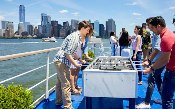 People playing foosball on a New York dinner cruise with skyline view.