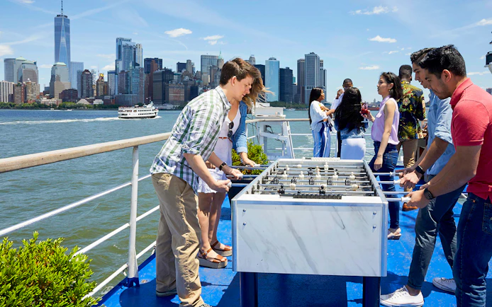 People playing foosball on a New York dinner cruise with skyline view.