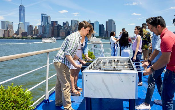 People playing foosball on a New York dinner cruise with skyline view.