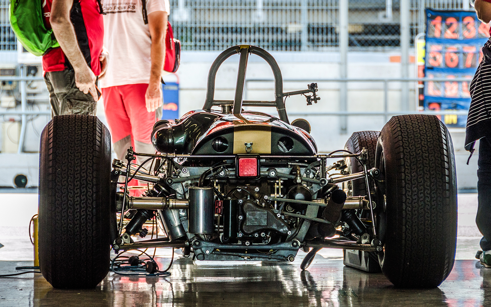 Race car in garage at Montjuïc Park Circuit with people nearby.