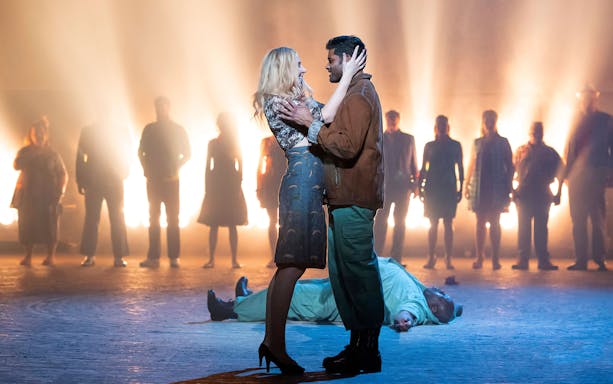 Couple embracing on stage during Carmen performance with cast in background.
